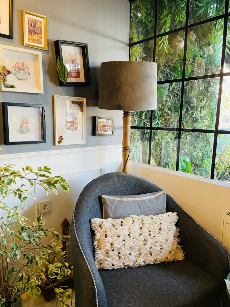 Espaço com cadeira cinza, almofada de flores e iluminária de chão.