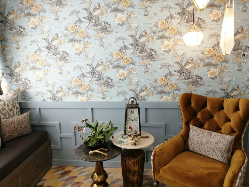 Sala de estar com estilo vintage na decoração: poltrona antiga aveludada, papel de parede floral e relógio de mesa no formato lanterna.
