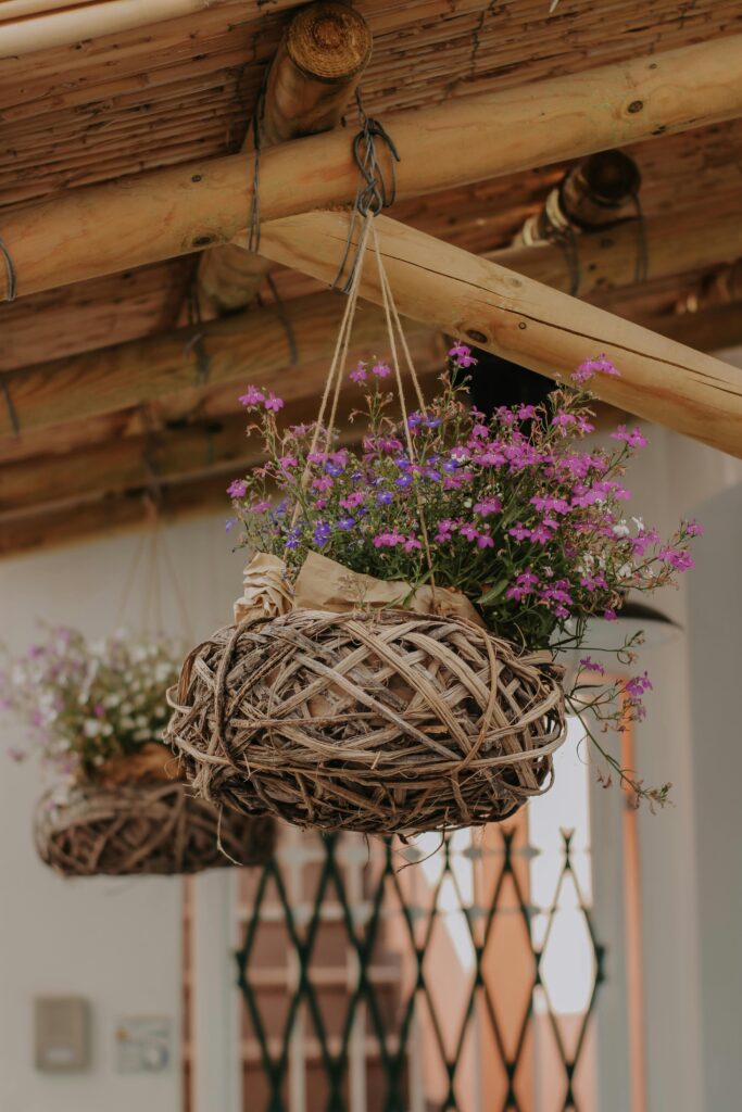 Cachepôs de palha suspensos, com flores em uma área externa.
