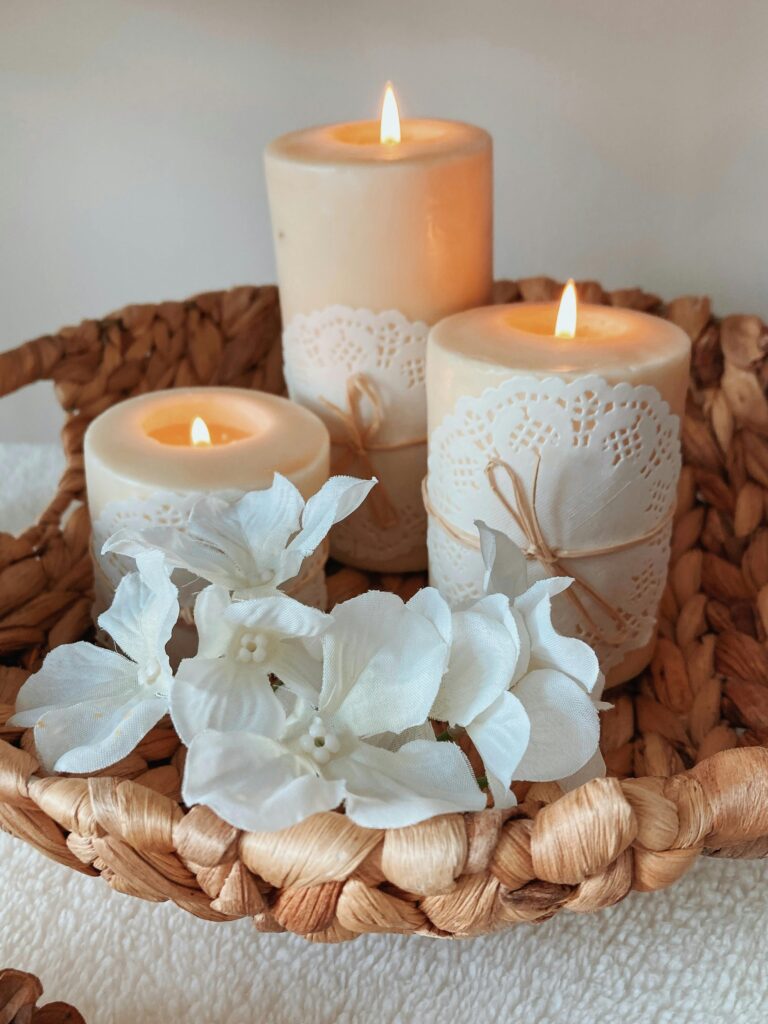 Velas de tamanhos diferentes decoradas e acessas sobre uma cesta de palha.