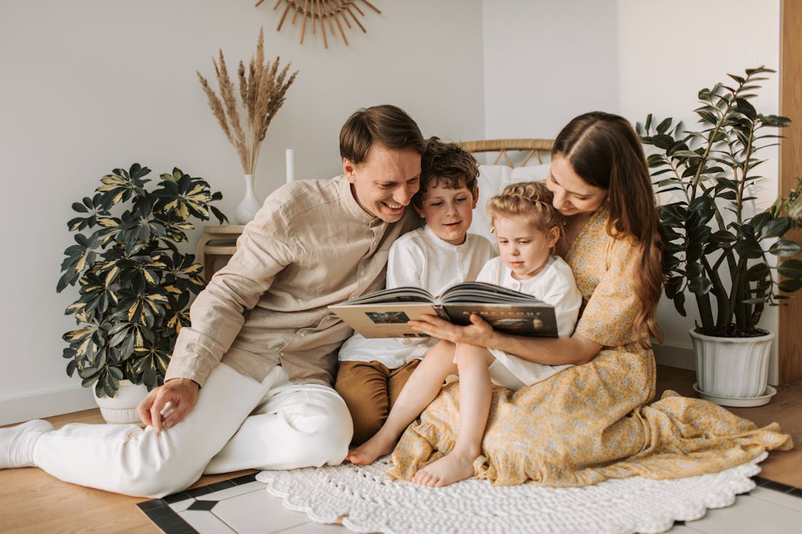 Família unida em um momento de leitura no lar, sentados no chão em um ambiente acolhedor com decoração boho, transmitindo harmonia, carinho e simplicidade.