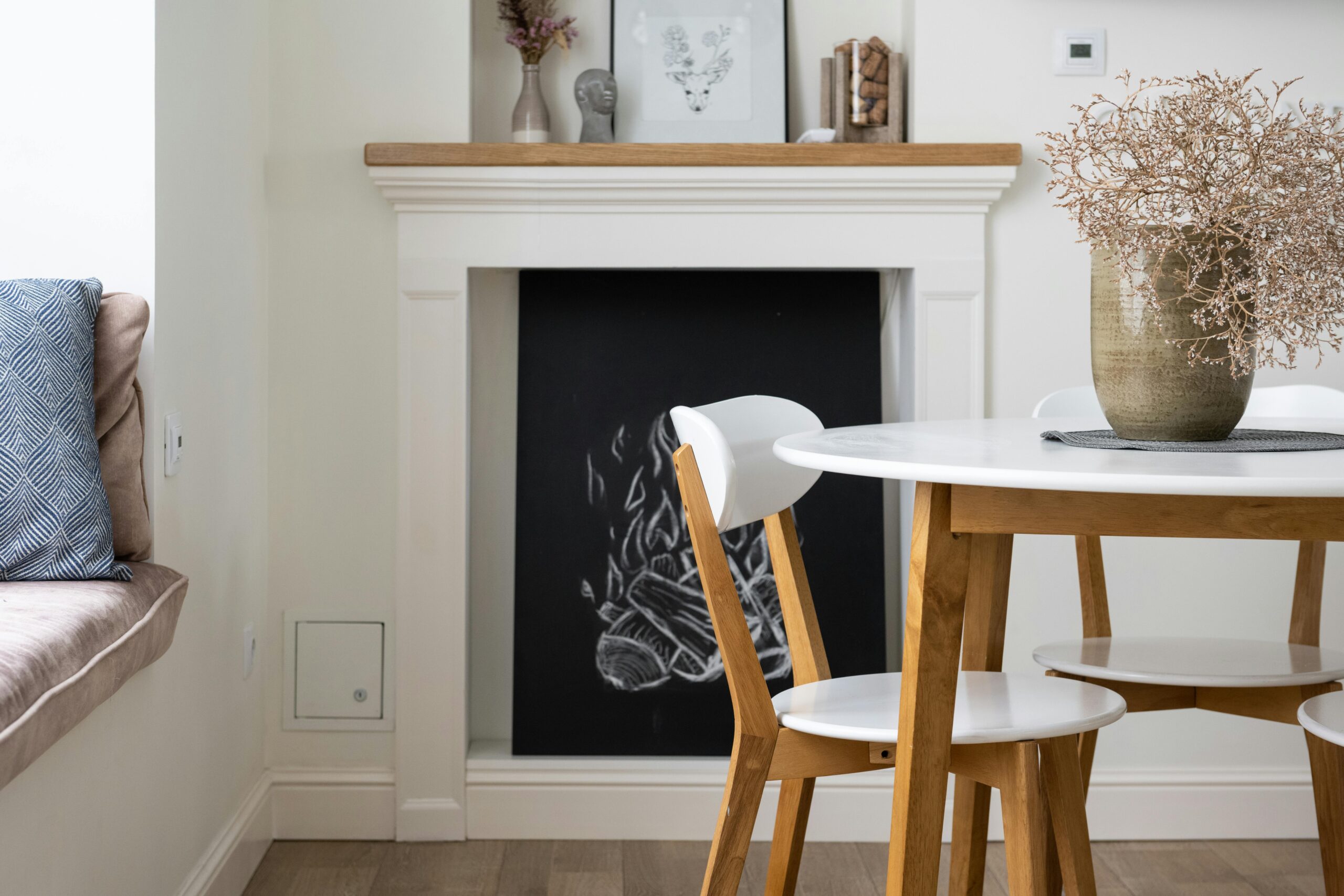 Sala de jantar com mesa branca e vaso de galhos secos em ambiente claro, com decoração natural e acolhedora