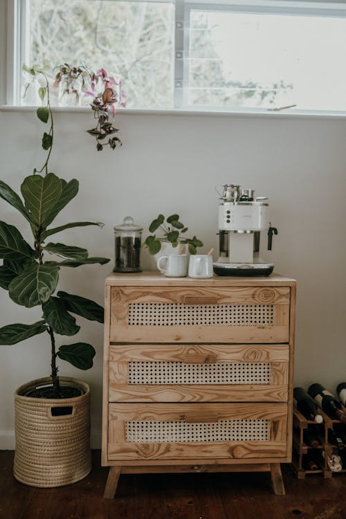 Cantinho do café em casa com cômoda de madeira rústica, cafeteira branca, xícaras e plantas, no estilo boho com toques naturais.