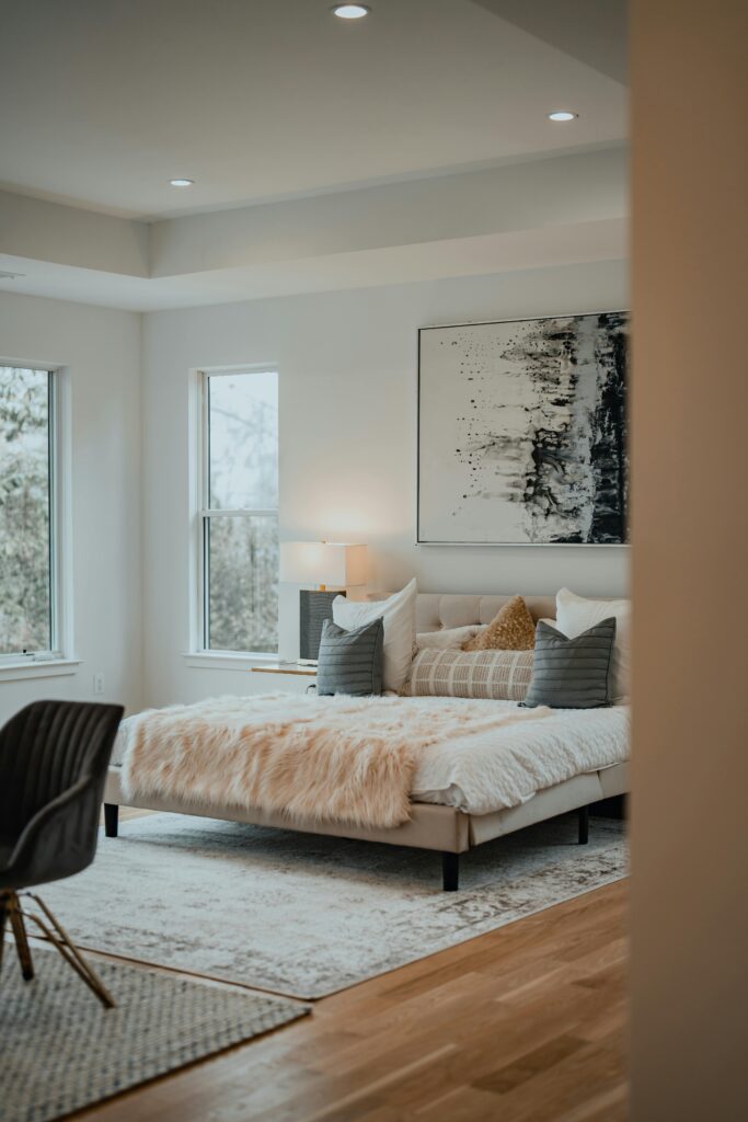 Quarto decorado no estilo escandinavo, com cama clara, manta em tricô, cadeira creme e parede com ripado de madeira, criando um ambiente minimalista, elegante e aconchegante.