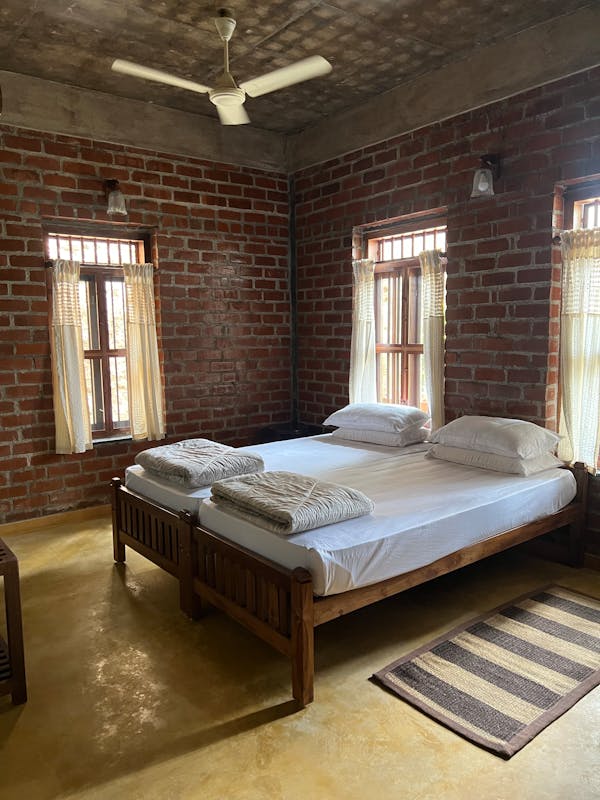 Quarto rústico com cama de madeira, paredes de tijolos aparentes e luz natural.