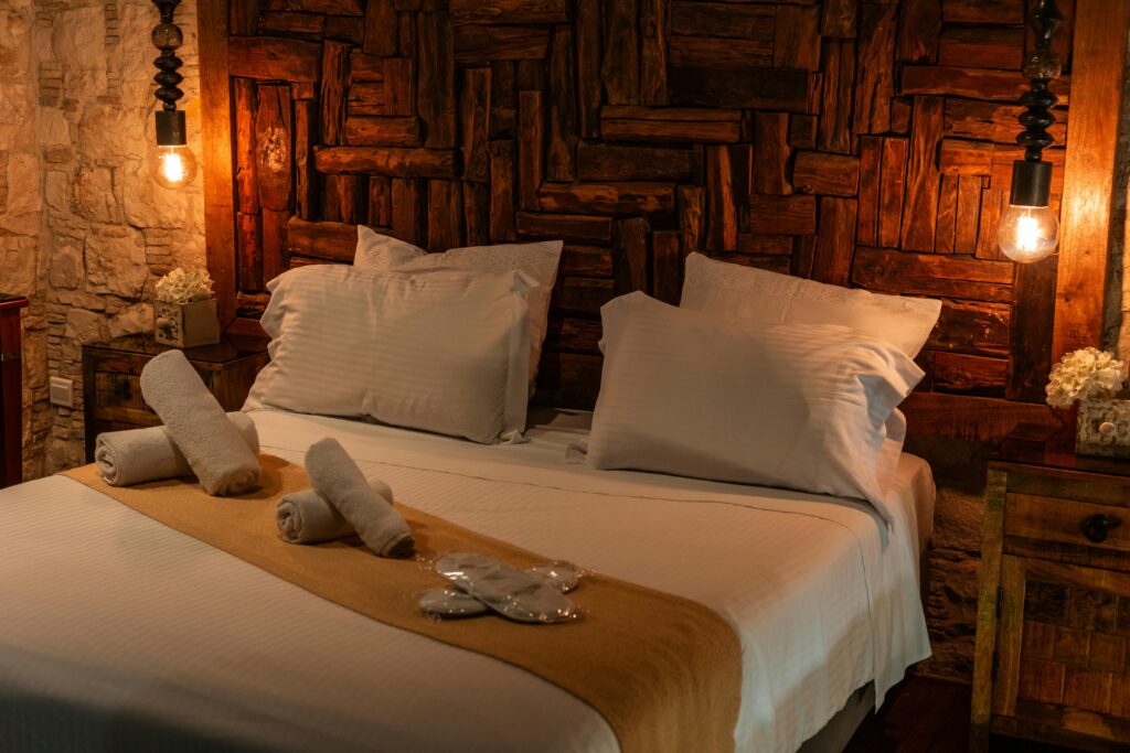 Quarto rústico com iluminação suave, cabeceira de madeira entalhada e detalhes artesanais.