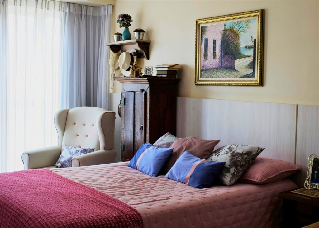 Quarto pequeno com poltrona confortável, almofadas coloridas e decoração com móveis antigos, para demonstrar como organizar um quarto pequeno. 
