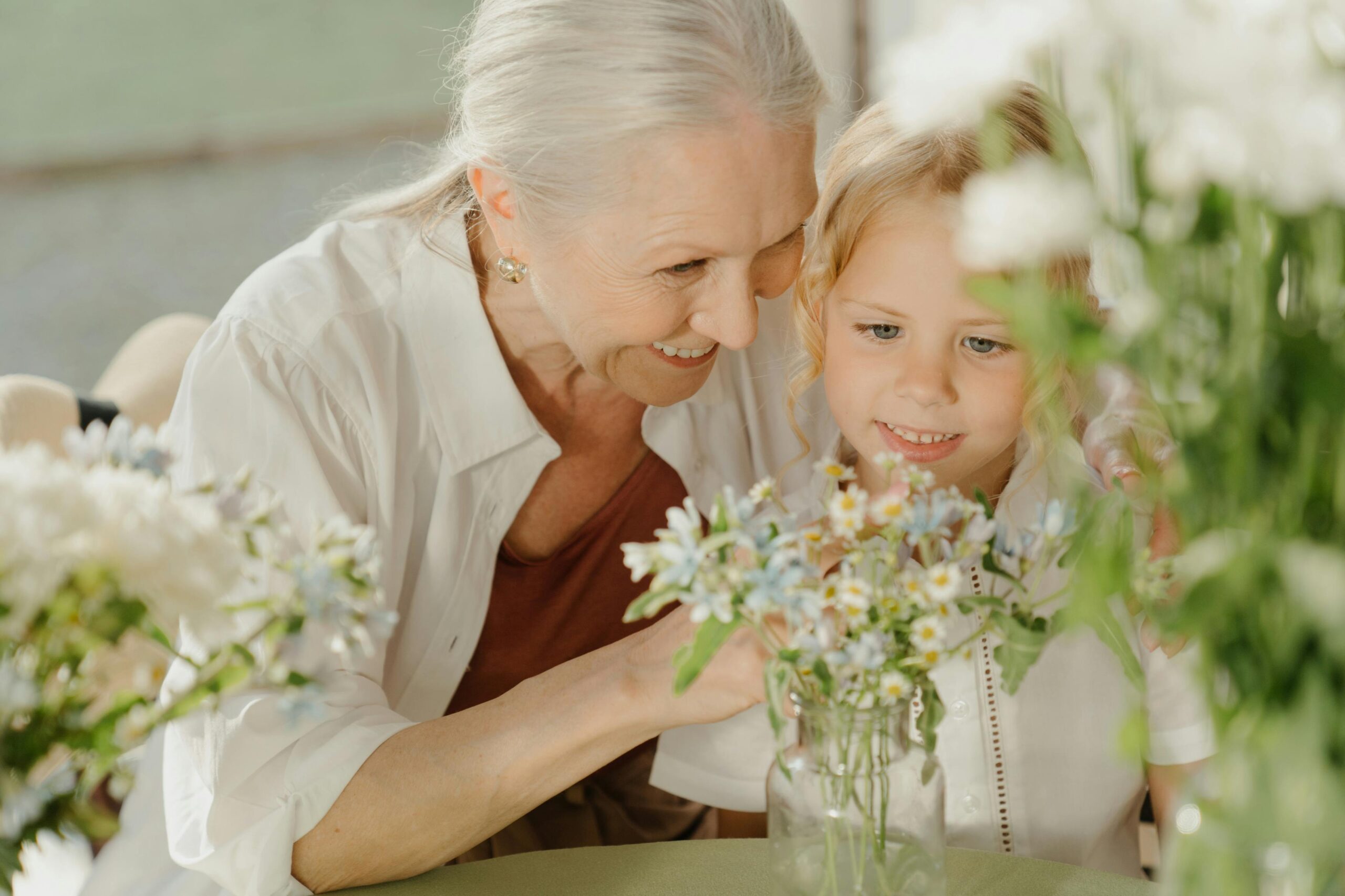 Idosa feliz em casa adaptada, segurando flores e sorrindo com tranquilidade.