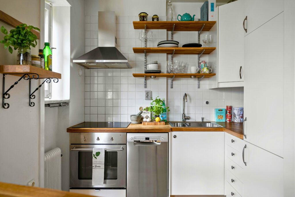 Organização da cozinha pequena com armários brancos e prateleiras de madeira bem distribuídas.