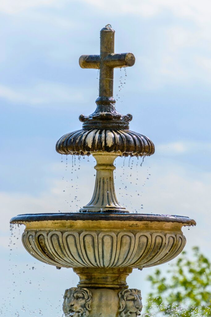 Fonte de água decorativa clássica com cruz no topo, símbolo de fé e contemplação