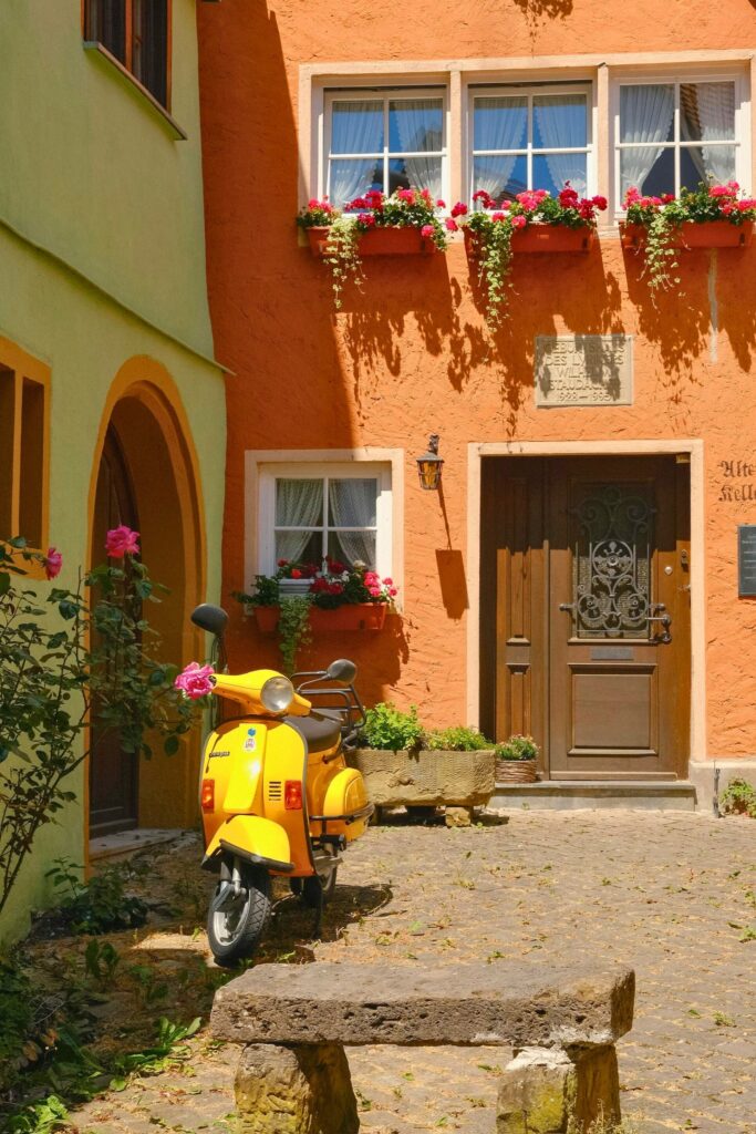 entrada de casa italiana com fachada em tons terrosos, porta de madeira e Vespa amarela decorando a cena