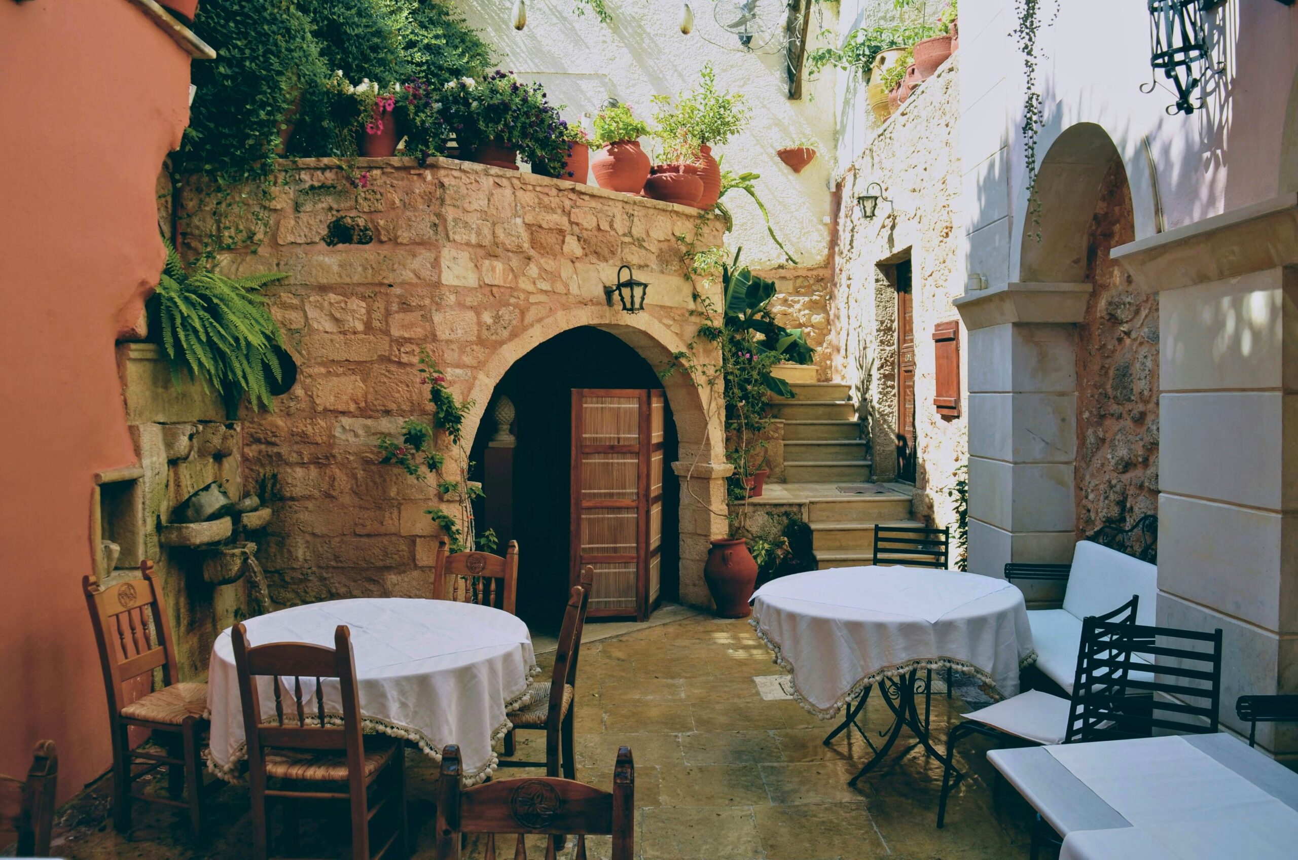 Pátio de casa italiana com mesas simples, vasos e arcos em pedra, representando a dolce vita no cotidiano.