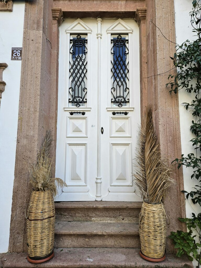  porta branca clássica com moldura em pedra e vasos de palha na entrada