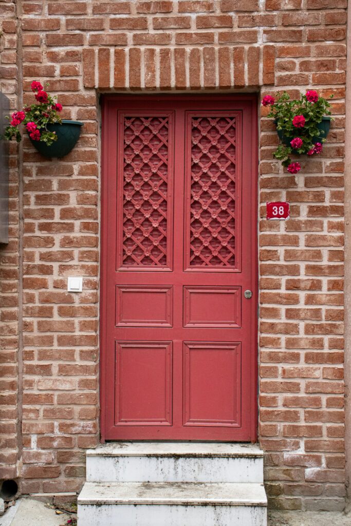 porta vermelha em fachada de tijolos com vasos floridos