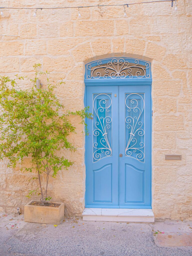 Portas azuis na entrada da casa com parede de pedra clara e planta lateral